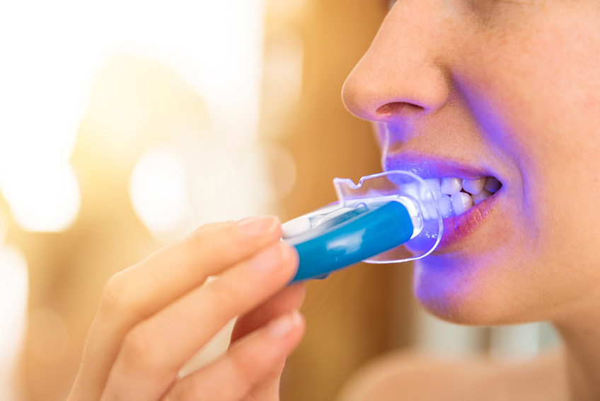 Woman is whitening teeth with LED light